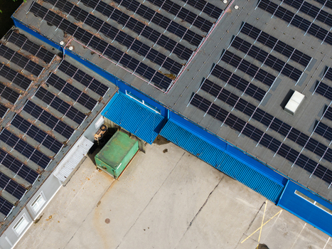 Aerial view of a commercial building roof covered with solar panels featuring blue metal trim and a green container on the concrete yard below in Riga Latvia. Aerial view of a commercial building roof covered with solar panels featuring blue metal trim and a green container on the concrete yard below in Riga Latvia.