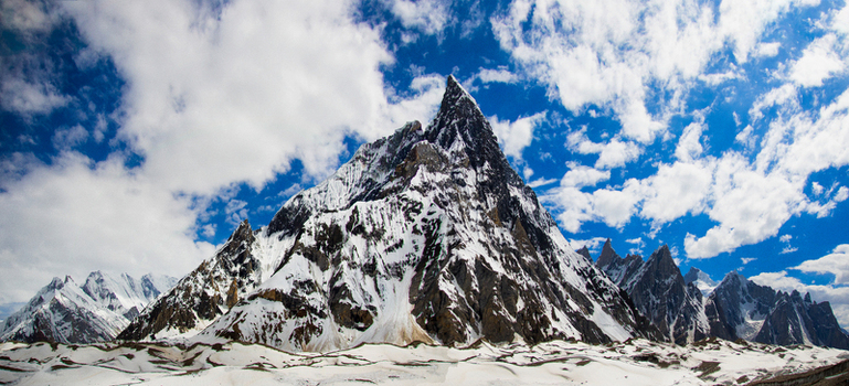 View of the sharp snow covered summit of Mitre Peak under a bright blue sky with white clouds in Skardu Gilgit Pakistan.