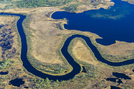 Aerial view of Tufsingdeltaet featuring a winding river flowing through dark blue water and vast marshy wetlands in Tufsingdalen Innlandet Norway. Aerial view of Tufsingdeltaet featuring a winding river flowing through dark blue water and vast marshy wetlands in Tufsingdalen Innlandet Norway.
