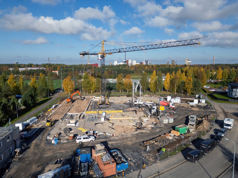 Oulu Finland 25 September 2026 Aerial view of a construction site featuring a yellow tower crane heavy machinery foundation work and surrounding autumn trees under a blue sky.