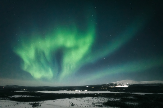 Aerial view of the Aurora Borealis illuminating the night sky over the snow covered landscape and distant mountain in Yllasjarvi Lapland Finland.