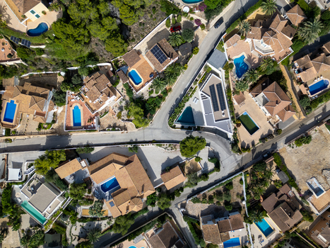 Aerial view of residential villas with swimming pools terracotta roofs and lush greenery in a coastal neighborhood in Moraira Valencian Community Spain.