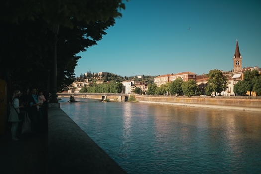 View of the Adige River flowing through the historic city center with colorful buildings and a church spire under a clear blue sky in Verona Veneto Italy.