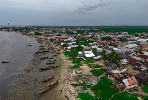 Aerial view of Bonny Island featuring a coastal town with numerous wooden boats moored along the sandy shoreline residential buildings and lush greenery in Bonny Town Rivers Nigeria. Aerial view of Bonny Island featuring a coastal town with numerous wooden boats moored along the sandy shoreline residential buildings and lush greenery in Bonny Town Rivers Nigeria.
