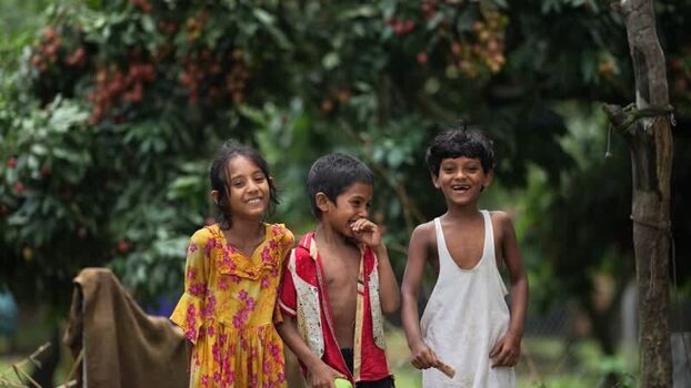 View of three children laughing in a lychee orchard in Bangladesh.