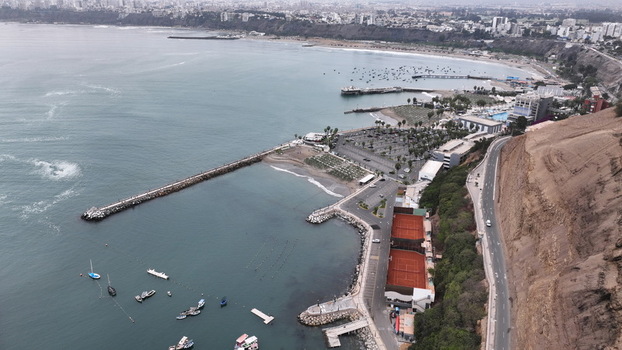 Aerial view of the coastline featuring a long pier small boats in the bay red clay tennis courts and steep cliffs along the Pacific Ocean in Chorrillos Lima Province Peru.