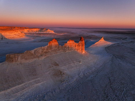 Aerial view of the stark sun kissed rock formations jutting from the pale earth under a fiery sunset sky Aktau Mangystau Kazakhstan.