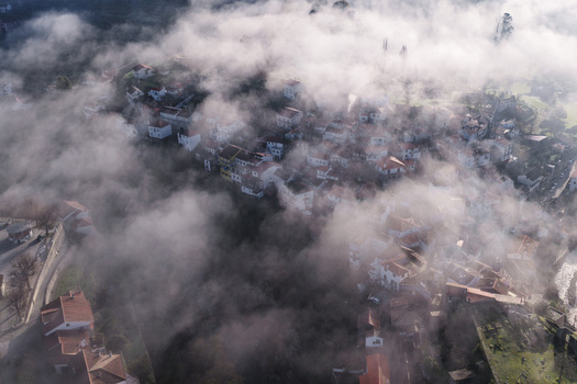 Aerial view of the historic village of Avo shrouded in thick morning mist with red tiled rooftops peeking through the clouds in Oliveira do Hospital Coimbra District Portugal.