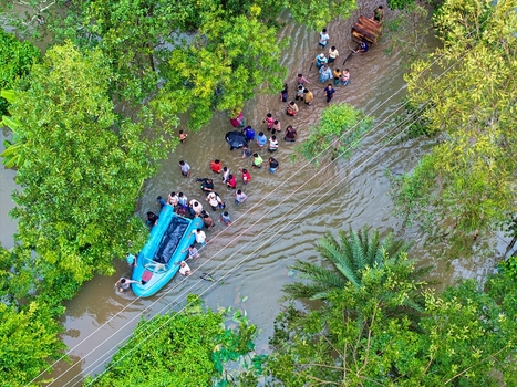 Banshkhali Upazila Chittagong Division Bangladesh 10 July 2026 Aerial view of a flooded road with people wading through water and a small boat amidst lush green trees. Banshkhali Upazila Chittagong Division Bangladesh 10 July 2026 Aerial view of a flooded road with people wading through water and a small boat amidst lush green trees.