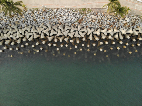 Aerial view of concrete tetrapods forming a breakwater along the coastline with a paved walkway and palm trees in La Cruz de Huanacaxtle Nayarit Mexico. Aerial view of concrete tetrapods forming a breakwater along the coastline with a paved walkway and palm trees in La Cruz de Huanacaxtle Nayarit Mexico.