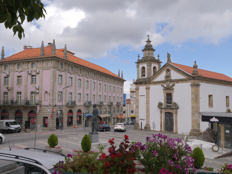 View of the historic square featuring a traditional church a large pink building a central statue and vibrant flowers in the foreground in Covilha Castelo Branco District Portugal.