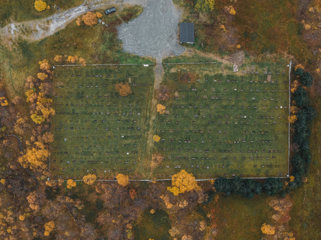 Aerial view of a cemetery in Senja surrounded by autumn trees and green grass in Senja Troms Norway.