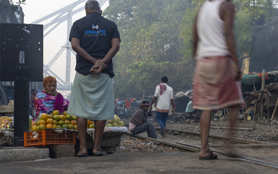 Kolkata India 05 December 2024 View of the Howrah Bridge looming in the background as locals gather near the railway tracks their vibrant clothing contrasting with the industrial landscape. Kolkata India 05 December 2024 View of the Howrah Bridge looming in the background as locals gather near the railway tracks their vibrant clothing contrasting with the industrial landscape.