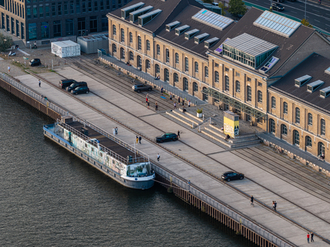 Aerial view of Spreespeicher Promenade along the Spree river featuring a historic industrial building a moored boat and people walking on the waterfront. Berlin Berlin Germany. Aerial view of Spreespeicher Promenade along the Spree river featuring a historic industrial building a moored boat and people walking on the waterfront. Berlin Berlin Germany.