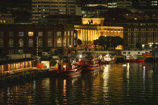 View of red tugboats docked at the harbour with the illuminated Wellington Railway Station in the background at night in Wellington Wellington Region New Zealand.