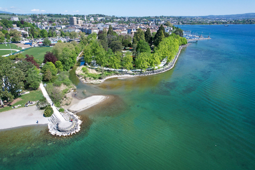 Aerial view of the lush green trees of Parc de l Independance along the turquoise waters of Lake Geneva in Morges Vaud Switzerland. Aerial view of the lush green trees of Parc de l Independance along the turquoise waters of Lake Geneva in Morges Vaud Switzerland.