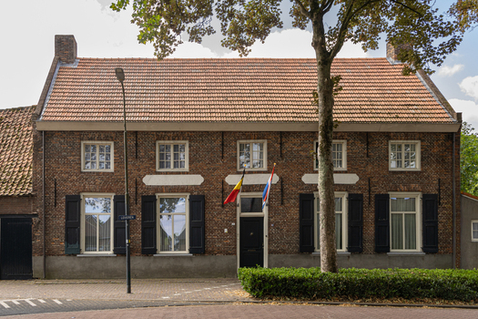 View of a traditional brick house with a tiled roof black shutters and flags displayed at the entrance in Baarle Nassau North Brabant Netherlands.