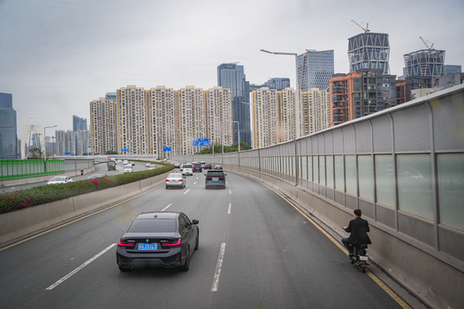 Guangzhou China 23 February 2024 View of traffic on a highway with a person riding a scooter on the shoulder and modern skyscrapers in the background. Guangzhou China 23 February 2024 View of traffic on a highway with a person riding a scooter on the shoulder and modern skyscrapers in the background.