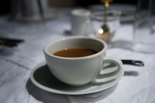 View of a white ceramic coffee cup on a saucer placed on a white tablecloth in Point Roberts Washington United States.