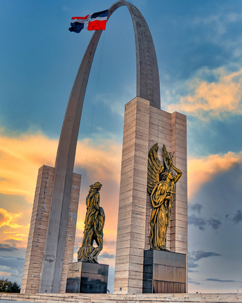 View of the iconic arch and golden statues of the Plaza de la Bandera against a dramatic sunset sky in Santo Domingo Santo Domingo Provinc Dominican Republic.
