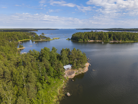 Aerial view of a small cabin nestled in a dense pine forest on a rocky coastline surrounded by the calm blue waters of the Gulf of Finland in Hamina Kymenlaakso Finland. Aerial view of a small cabin nestled in a dense pine forest on a rocky coastline surrounded by the calm blue waters of the Gulf of Finland in Hamina Kymenlaakso Finland.
