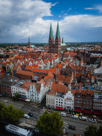Aerial view of red rooftops cascading towards the Trave River juxtaposed against the towering twin spires of the Marienkirche L&uuml;beck Schleswig Holstein Germany.