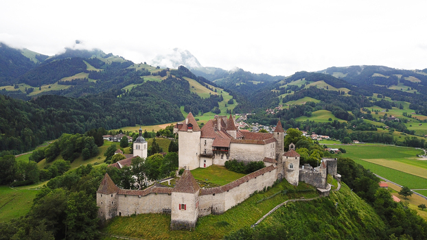 Aerial view of Chateau de Gruyeres with its stone walls and towers overlooking the lush green alpine landscape and rolling hills Gruyeres Fribourg Switzerland.