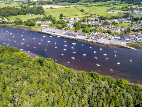 Aerial view of the River Moy with numerous small boats moored along the bank surrounded by lush green trees and residential houses in Ballina County Mayo Ireland.
