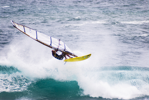 View of a windsurfer performing a jump over a breaking wave in the ocean off the coast of Kauai Kauai County Hawaii United States.