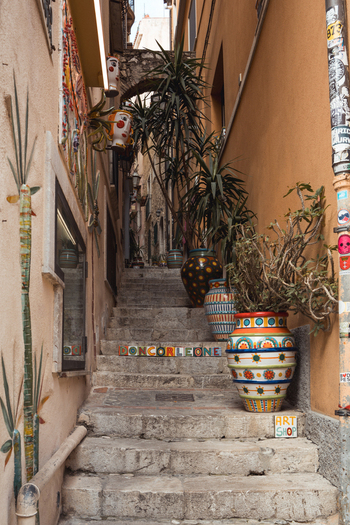 View of aged stone steps adorned with vibrant ceramic tiles and lush potted plants ascending through narrow alleyways Taormina Sicily Italy.