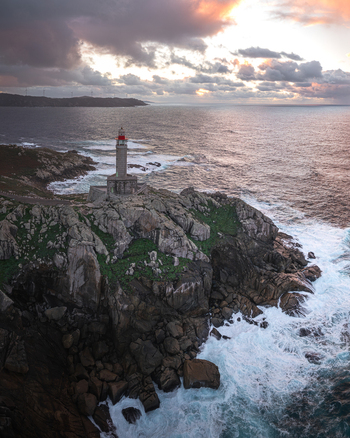Aerial view of Faro de Punta Nariga lighthouse standing on a rugged rocky cliff with crashing waves and a dramatic sunset sky Malpica A Coruna Spain. Aerial view of Faro de Punta Nariga lighthouse standing on a rugged rocky cliff with crashing waves and a dramatic sunset sky Malpica A Coruna Spain.