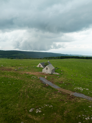 Aerial view of stone buildings nestled in vibrant green fields beneath a brooding sky Nasbinals Occitanie France. Aerial view of stone buildings nestled in vibrant green fields beneath a brooding sky Nasbinals Occitanie France.