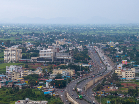 Aerial view of the highway passing through the town with surrounding buildings lush green fields and vehicles on the road in Karad Maharashtra India.