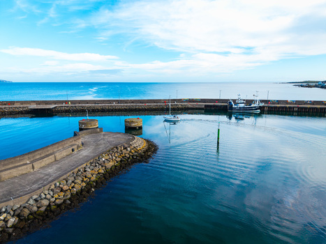 Aerial view of Bangor Harbour with a small sailboat and a fishing vessel in the calm blue water surrounded by stone breakwaters in Bangor Northern Ireland United Kingdom.