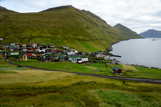 View of a small coastal village with colorful houses nestled between lush green mountains and the sea in the Faroe Islands. View of a small coastal village with colorful houses nestled between lush green mountains and the sea in the Faroe Islands.