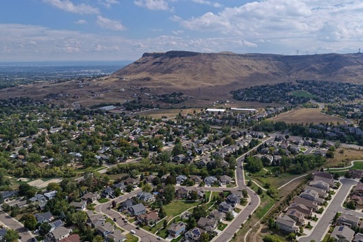 Aerial view of North Table Mountain rising above a suburban residential neighborhood with green trees and houses in Golden Colorado United States.