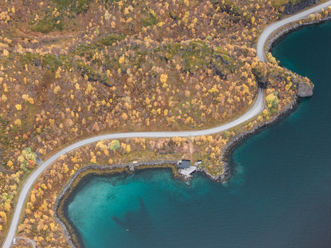 Aerial view of the winding coastal road surrounded by vibrant autumn foliage and deep blue waters along the rugged shoreline in Senja Troms Norway.
