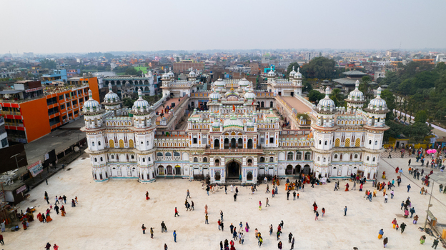 Aerial view of the ornate Janaki Mandir temple complex with its white domes and intricate architecture surrounded by a bustling courtyard and urban landscape in Nepal.