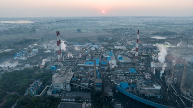 Aerial view of an industrial factory complex in Nagda with tall smokestacks emitting smoke under a hazy sunset sky in Nagda Madhya Pradesh India. Aerial view of an industrial factory complex in Nagda with tall smokestacks emitting smoke under a hazy sunset sky in Nagda Madhya Pradesh India.