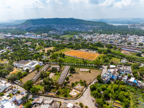 Aerial view of the urban landscape of Udaipur featuring green trees residential buildings an open field and railway tracks stretching across the city in Udaipur Rajasthan India. Aerial view of the urban landscape of Udaipur featuring green trees residential buildings an open field and railway tracks stretching across the city in Udaipur Rajasthan India.