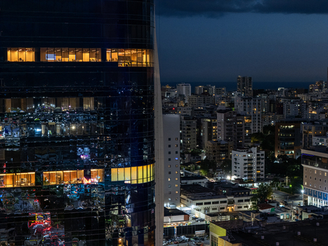 Aerial view of a modern glass skyscraper with illuminated office windows at night overlooking the dense urban skyline of Santo Domingo Distrito Nacional Dominican Republic. Aerial view of a modern glass skyscraper with illuminated office windows at night overlooking the dense urban skyline of Santo Domingo Distrito Nacional Dominican Republic.