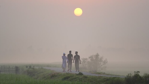 View of three men walking on a rural road at sunrise Bangladesh.