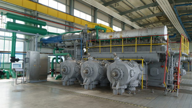 View of a large industrial gas compressor engine with green yellow and blue pipes in a facility in Latvia. View of a large industrial gas compressor engine with green yellow and blue pipes in a facility in Latvia.