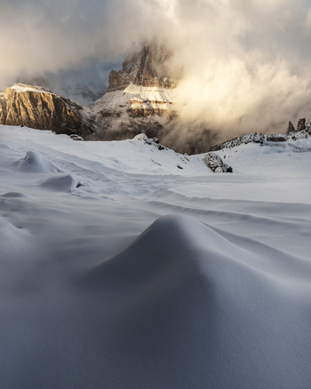 View of the Dolomites peaks emerging from thick clouds above a pristine snow covered field in Trentino Alto Adige Italy. View of the Dolomites peaks emerging from thick clouds above a pristine snow covered field in Trentino Alto Adige Italy.