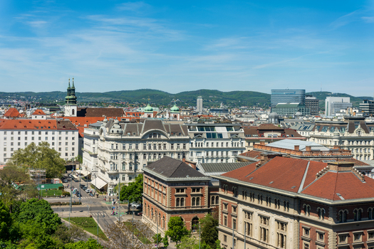 Aerial view of historic architecture with red tiled rooftops church spires and lush green hills under a clear blue sky in Vienna Vienna Austria. Aerial view of historic architecture with red tiled rooftops church spires and lush green hills under a clear blue sky in Vienna Vienna Austria.