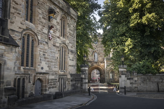 View of the historic stone architecture and arched gatehouse of Durham Castle surrounded by lush green trees in Durham England United Kingdom. View of the historic stone architecture and arched gatehouse of Durham Castle surrounded by lush green trees in Durham England United Kingdom.