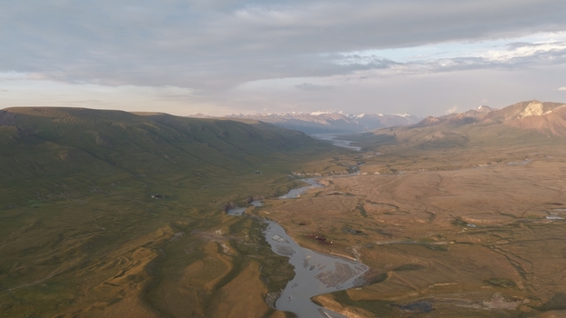 Aerial view of the Enilchek river winding through the vast grassy valley surrounded by rugged mountains under a dramatic sky in Enilchek Issyk Kul Region Kyrgyzstan. Aerial view of the Enilchek river winding through the vast grassy valley surrounded by rugged mountains under a dramatic sky in Enilchek Issyk Kul Region Kyrgyzstan.