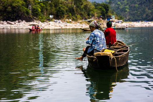 Meghalaya India 31 March 2023 View of two women sitting in a traditional wooden boat on the calm river with lush green hills in the background. Meghalaya India 31 March 2023 View of two women sitting in a traditional wooden boat on the calm river with lush green hills in the background.