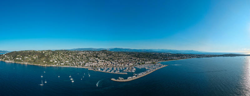 Aerial view of the marina and coastline of Antibes with boats docked in the harbor surrounded by buildings and hills under a clear blue sky in Antibes Provence Alpes Cote d Azur France. Aerial view of the marina and coastline of Antibes with boats docked in the harbor surrounded by buildings and hills under a clear blue sky in Antibes Provence Alpes Cote d Azur France.