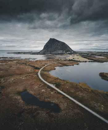 Aerial view of Gimsoy mountain rising above the rugged coastal landscape with a winding road dark lakes and dramatic cloudy sky Vagan Municipality Nordland Norway. Aerial view of Gimsoy mountain rising above the rugged coastal landscape with a winding road dark lakes and dramatic cloudy sky Vagan Municipality Nordland Norway.